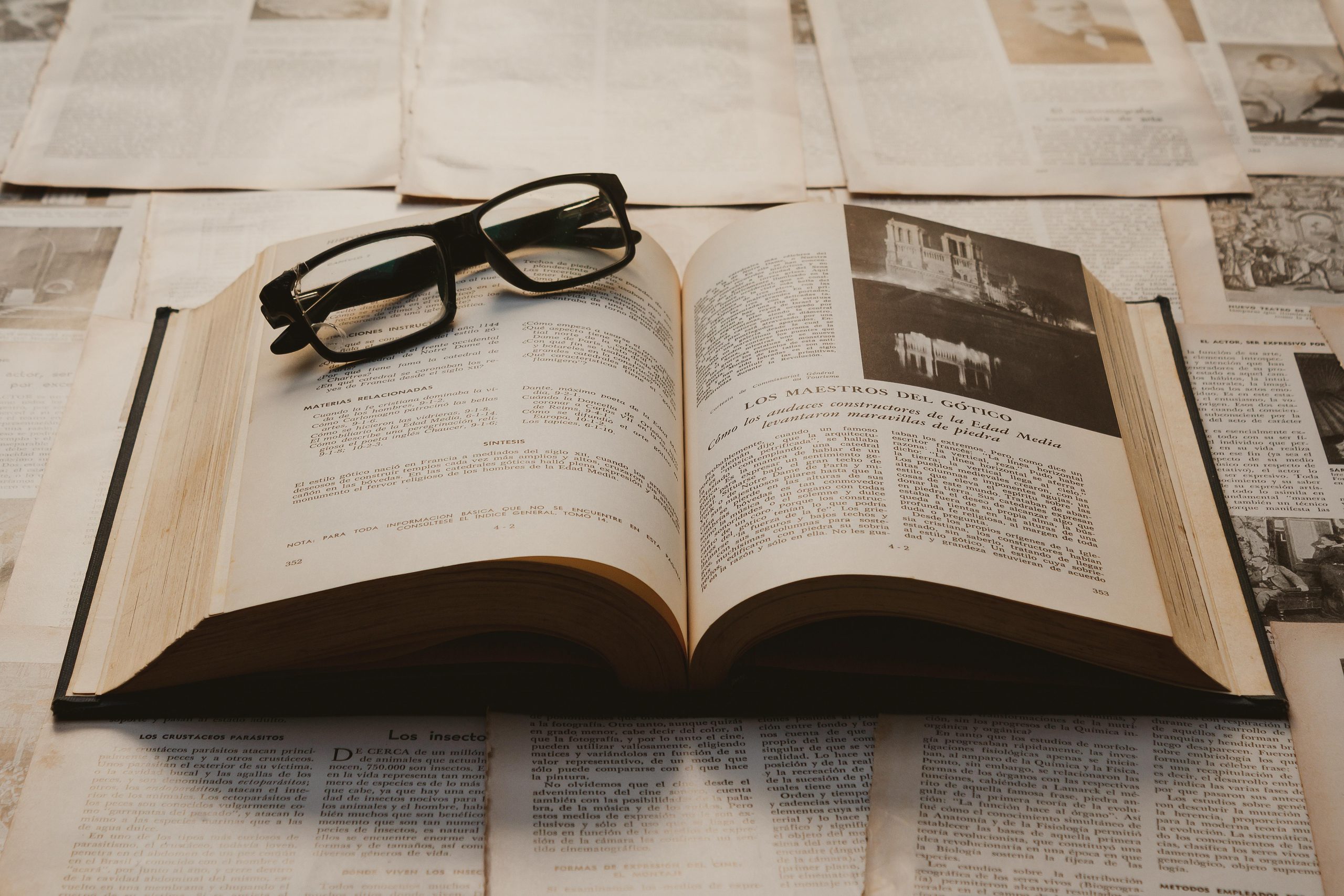 A vintage book open on a table, surrounded by old papers, with resting glasses.